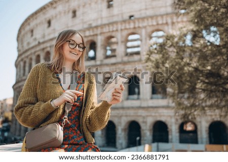 A happy blond woman tourist is standing near the Coliseum, old ruins at the center of Rome, Italy. Concept of traveling famous landmarks. Girl with map is walking on a sunny day