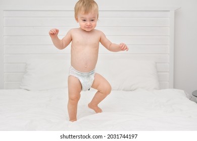 Happy blonde caucasian baby girl about 1 year old laughing jumping on white bedlinen in bedroom at home.Kid having fun before going to bed. Adorable child playing indoors on bed sheets.Selective focus