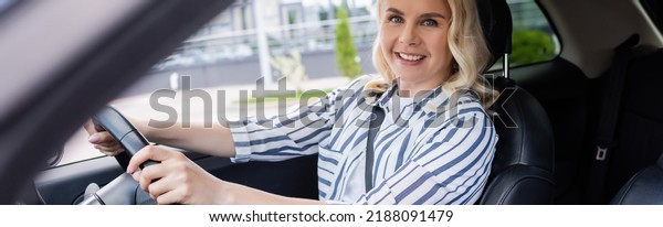 Happy blonde driver looking at camera during\
driving course in car,\
banner
