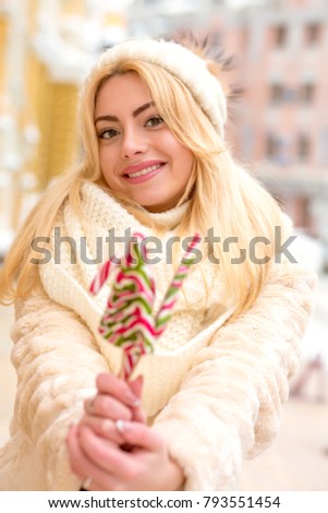 Happy blonde girl in warm hat and coat holding tasty Christmas sweets
