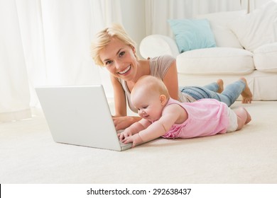 Happy blonde mother with her baby girl using laptop at home in the living room