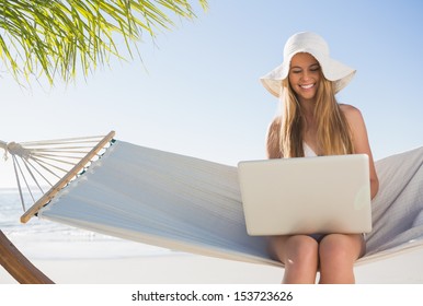 Happy Blonde Sitting On Hammock Using Laptop At The Beach