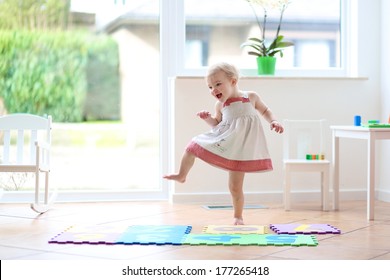 Happy blonde toddler girl having fun dancing indoors in a sunny white room at home or kindergarten