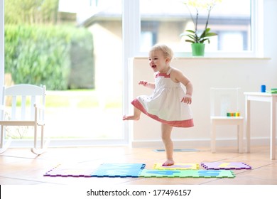 Happy Blonde Toddler Girl Having Fun Dancing Indoors In A Sunny White Room At Home Or Kindergarten