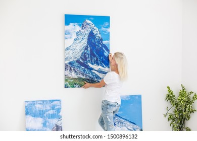 Happy Blonde Woman Hanging Large Picture On Wall At Home