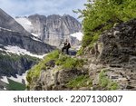 Happy blonde woman hiker stands on a cliff enjoying the view along the Grinnell Glacier Trail in Glacier National Park