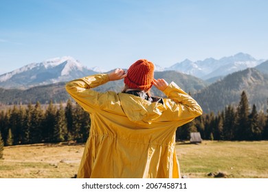 Happy Blonde Woman In Red Hat Standing Backwards Looking Away. Traveling In The Mountains. Freedom, Happiness, Travel And Vacations Concept, Outdoor Activities.