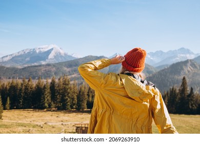 Happy Blonde Woman In Red Hat Standing Backwards Looking Away. Traveling In The Mountains. Freedom, Happiness, Travel And Vacations Concept, Outdoor Activities.