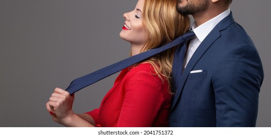 Happy blonde woman in red pulling rich man by necktie and smiling