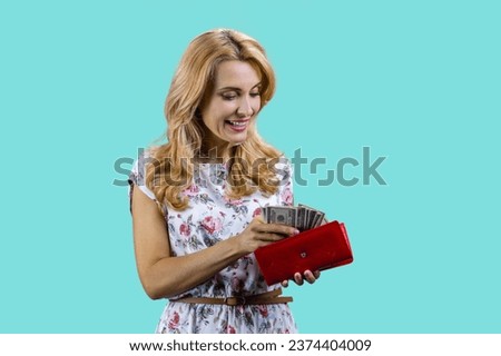 Happy blonde woman taking money from her wallet. Isolated on turquoise.