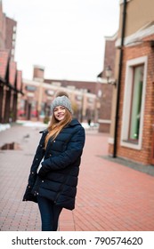 Happy Blonde Woman Wearing Black Winter Coat And Knitted Hat Posing At The Street In Kyiv