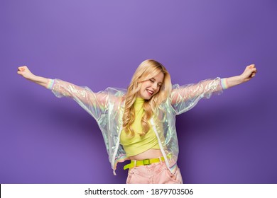 happy blonde young woman in colorful outfit with outstretched hands on purple background - Shutterstock ID 1879703506