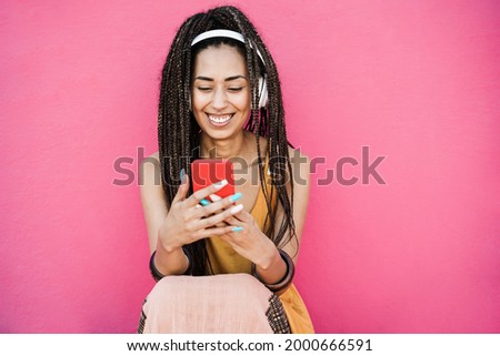 Happy bohemian influencer woman listening playlist music with pink background - Focus on face