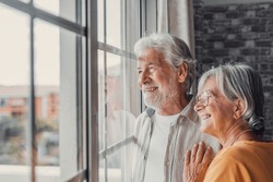 Happy Bonding Loving Middle Aged Senior Retired Couple Standing Near Window, Looking In Distance, Recollecting Good Memories Or Planning Common Future, Enjoying Peaceful Moment Together At Home.