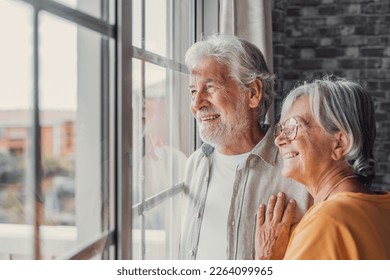 Happy bonding loving middle aged senior retired couple standing near window, looking in distance, recollecting good memories or planning common future, enjoying peaceful moment together at home. - Powered by Shutterstock