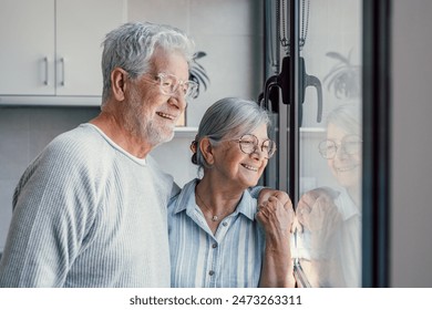 Happy bonding loving middle aged senior retired couple standing near window, looking in distance, recollecting good memories or planning common future, enjoying peaceful moment together at home. - Powered by Shutterstock