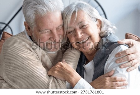 Happy bonding retired elderly couple sitting on sofa in a modern home relaxing and embracing, enjoying carefree moments together in good mood and harmony
