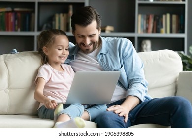 Happy Bonding Two Generations Family Relaxing On Comfortable Sofa, Watching Dunny Cartoons On Computer. Caring Young Father Teaching Little Preschool Daughter Using Modern Technology Device At Home.