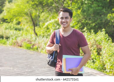 Happy bookworm. Handsome male student holding textbooks and smiling while standing at the outdoors