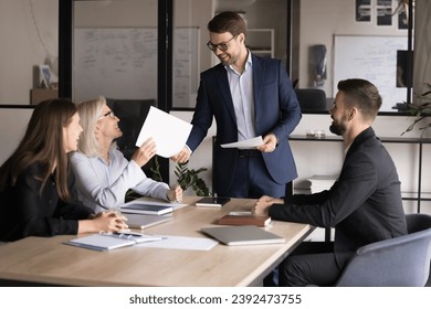 Happy boss holding meeting with business team, giving paper sales reports, certificate of gratitude to successful senior manager, colleague, employee, smiling, laughing - Powered by Shutterstock