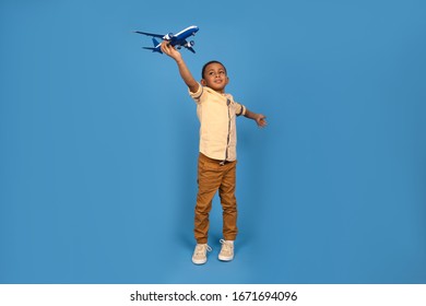 Happy boy African American in brown pants and a light shirt plays with a toy plane, imagines him flying in a plane against a blue background. Family travel and tourism, summer holidays consept. - Powered by Shutterstock