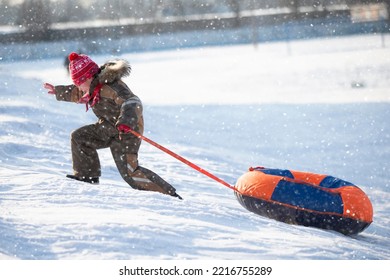 A happy boy up in the air on a tube sledding in the snow.. A boy slides down a hill in winter.