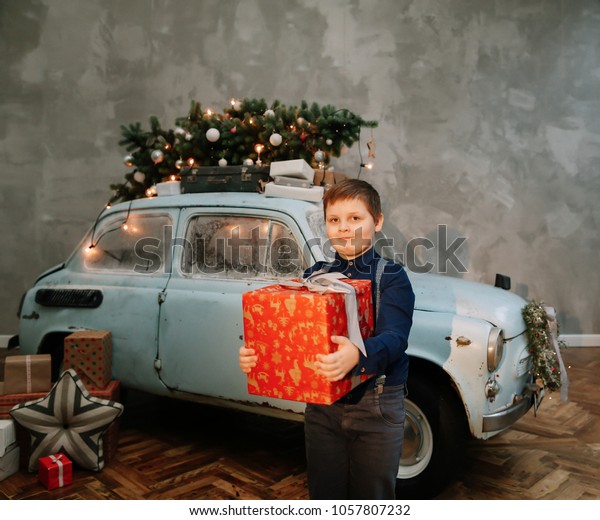 A happy boy and a blue car in the studio. Winter\
holidays concept.