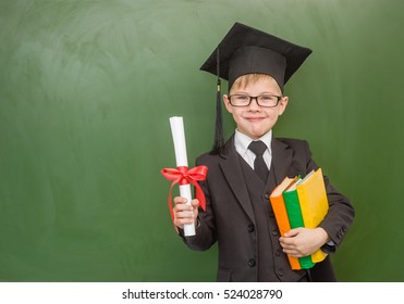 Happy boy with books and a diploma in graduation cap stands near a school board - Powered by Shutterstock