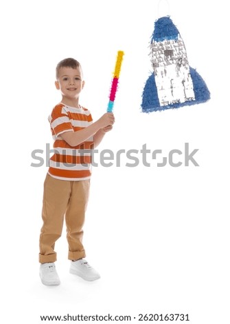 Happy boy breaking rocket shaped pinata with stick on white background