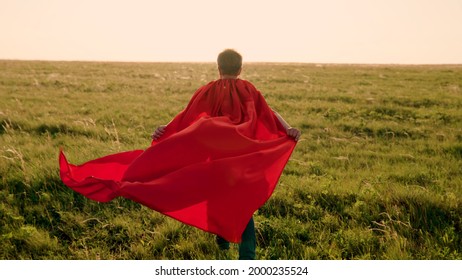 Happy boy, child superhero, runs across green field in red cloak, cloak flutters in wind. Childrens games, dreams. Slow motion. Teenager dreams of becoming superhero. Red cloak jerk, dream expression - Shutterstock ID 2000235524