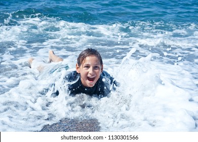 Happy Boy Covered With Foam Wave On Shingle Beach