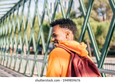 Happy Boy With Dark Skin In Tracksuit And With Backpack Walks On A Green Bridge