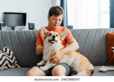 Happy boy with down syndrome relaxing on sofa and embracing his corgi dog at home. Love, animal concept - Powered by Shutterstock