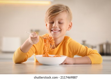 Happy boy eating tasty pasta at table in kitchen - Powered by Shutterstock