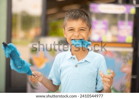 Happy boy eats blue cotton candy while visiting amusement park, spending summertime happily, Concept of entertainment and vacation
