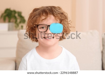 Happy boy with eye patch on glasses indoors. Strabismus treatment