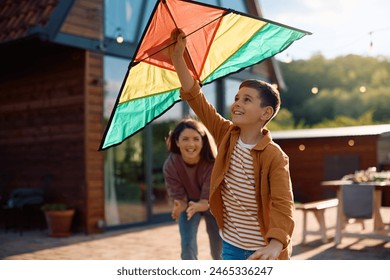 Happy boy flying a kite with mother's support outdoors. - Powered by Shutterstock