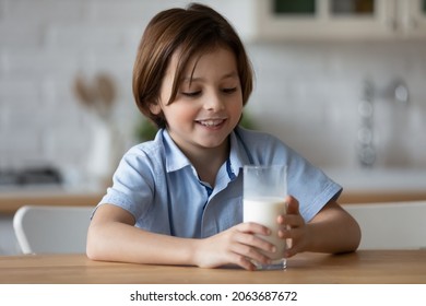 Happy boy with funny white moustache drinking milk in kitchen, holding glass, smiling. Cheerful kid keeping healthy diet nutrition, getting calcium, vitamins, probiotics for growth from dairy products - Powered by Shutterstock