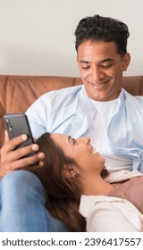 Happy boy and girl enjoy leisure relax activity at home laying and sitting on the sofa. Young male hispanic smile to a caucasian girl. Love and relationship people indoor lifestyle. Boy using phone - Shutterstock ID 2396417557