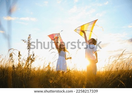 Happy boy and girl playing with kites in field at sunset. Happy childhood concept