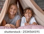 Happy boy and girl sitting in fort from blankets and smiling in camera. Siblings sister and brother playing together on the bed in the morning spending time weekend.