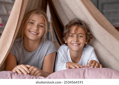 Happy boy and girl sitting in fort from blankets and smiling in camera. Siblings sister and brother playing together on the bed in the morning spending time weekend. - Powered by Shutterstock