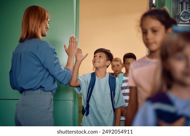 Happy boy giving high-five to his teacher while getting int he classroom with his classmates.  - Powered by Shutterstock