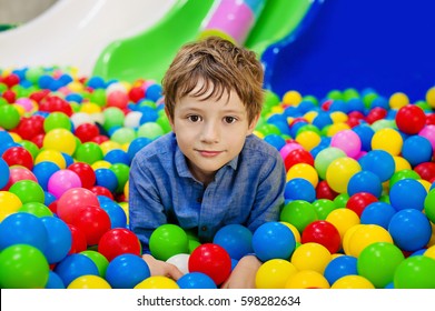 Happy Boy Having Fun In Ball Pit On Birthday Party In Kids Amusement Park And Indoor Play Center. Child Playing With Colorful Balls In Playground Ball Pool. Activity Toys For Little Kid