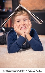 Happy boy having fun while lying on the carpet with book on his head.