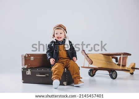 A happy boy in a helmet and a pilot's jacket stands near a wooden plane. Portrait of a child pilot, a child in a leather jacket. Wooden Toys. Eco plane from tree