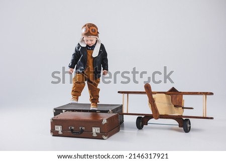 A happy boy in a helmet and a pilot's jacket stands near a wooden plane. Portrait of a child pilot, a child in a leather jacket. Wooden Toys. Eco plane from tree