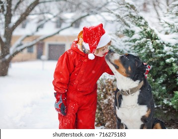 Happy Boy And His Black Dog In Winter In The Snow, Outdoor Games, Family, Best Friends, Smiling Kid And Large Swiss Mountain Dog On The Background Of  Winter Landscape, Winter Holidays, Christmas