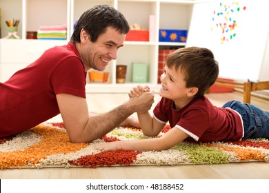 Happy Boy And His Father Arm Wrestling Laying On The Floor In The Kids Room