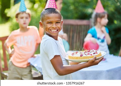 Happy Boy Holding Cake At Childrens Birthday Party In Summer In Garden